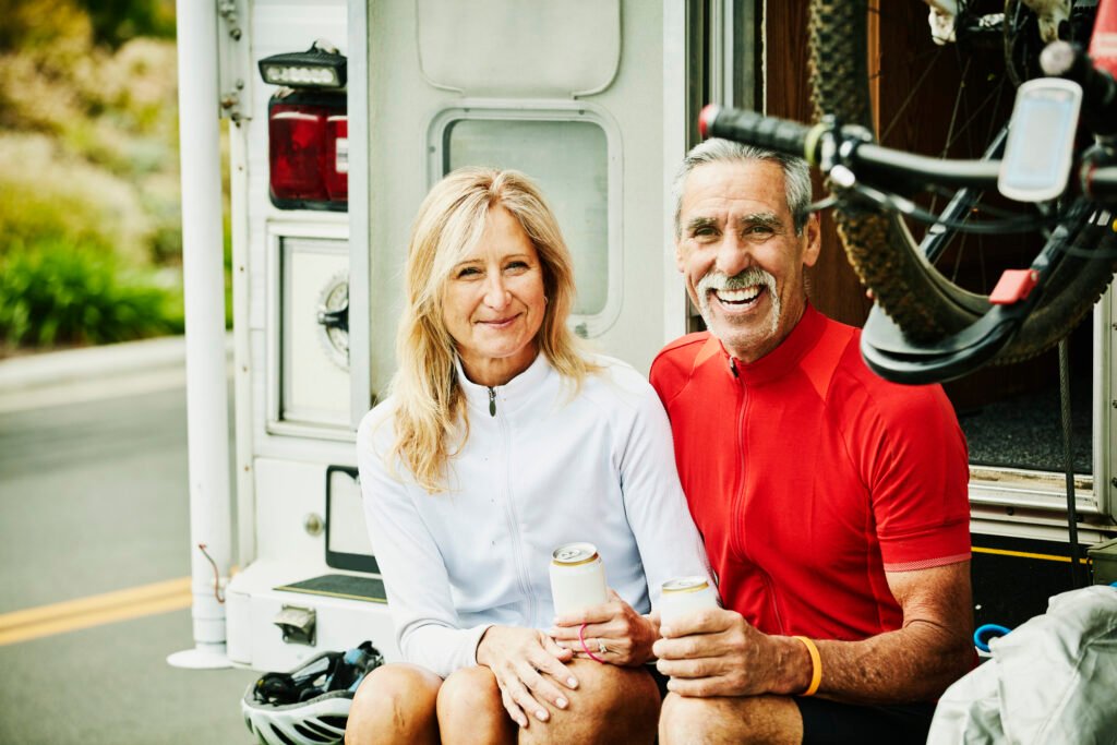 Smiling senior couple hanging out on back step of their RV after mountain bike ride