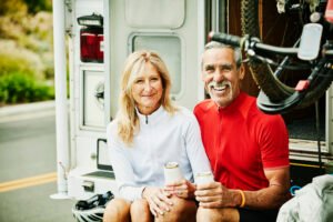 Smiling senior couple hanging out on back step of their RV after mountain bike ride