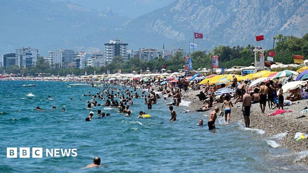 A beach in Turkey where lots of people are sunbathing under umbrellas, and many other people are swimming in the sea