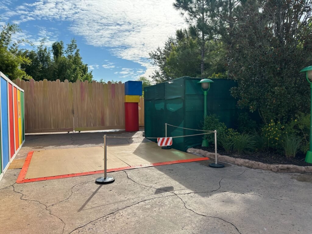 A woman and girl walk hand-in-hand toward the colorful entrance of Toy Story Land, surrounded by trees and greenery.