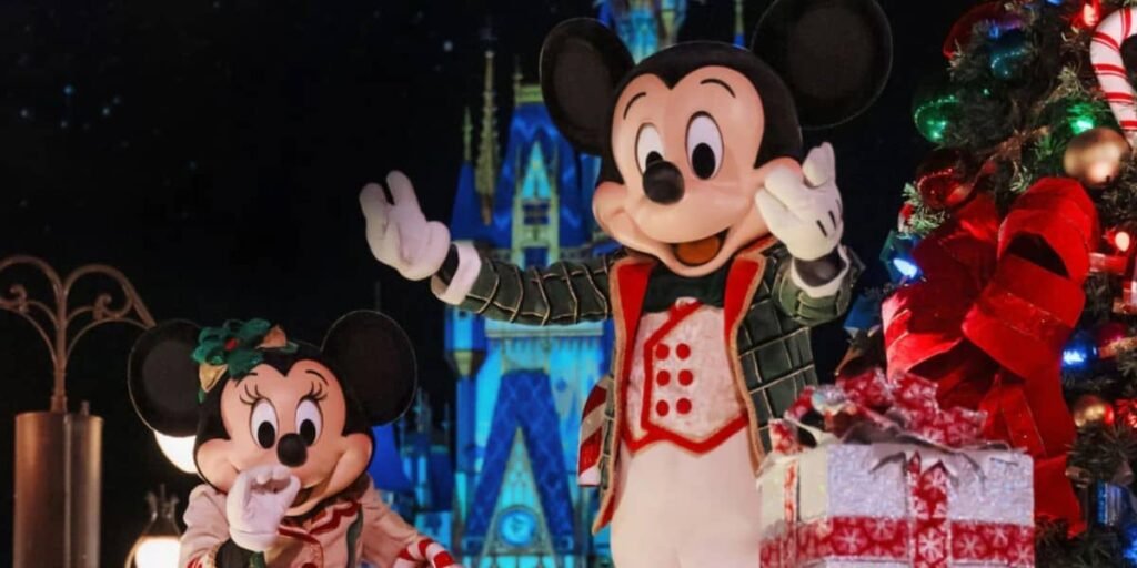 Mickey and Minnie Mouse dressed in festive holiday outfits stand near a decorated Christmas tree with wrapped gifts, enjoying the magical parade in front of a brightly lit castle at night.