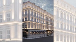 An elegant, light-colored multi-story building at dusk with classical detailing, warm exterior lighting, awnings, and two glass-canopy entrances along a quiet street.