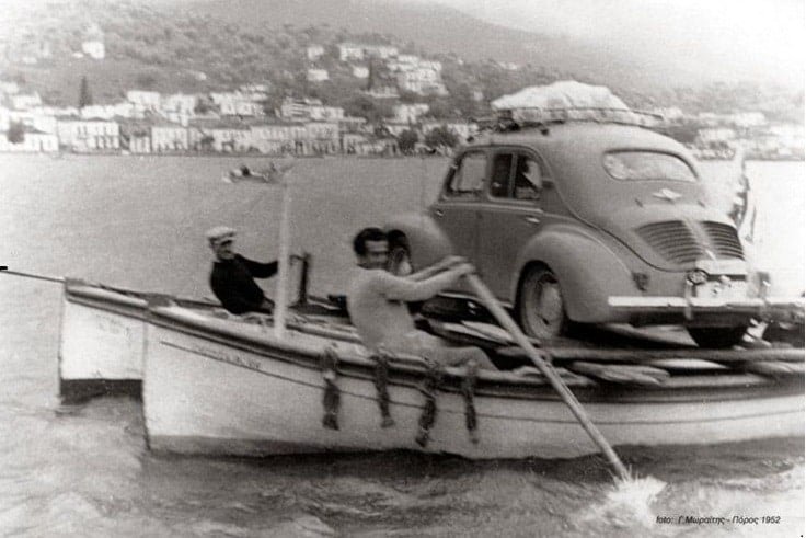 Two traditional fishing boat operators "ferry" a car from the island of Poros in Greece to the mainland in 1952