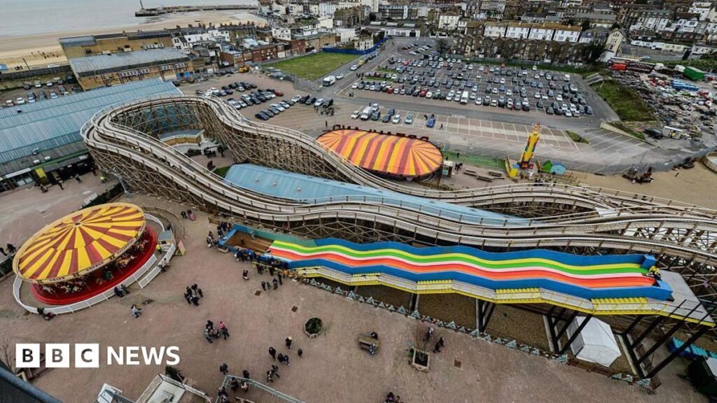 A top view of an amusement park. There are people wandering around the area. There is also a carousel and a ride.