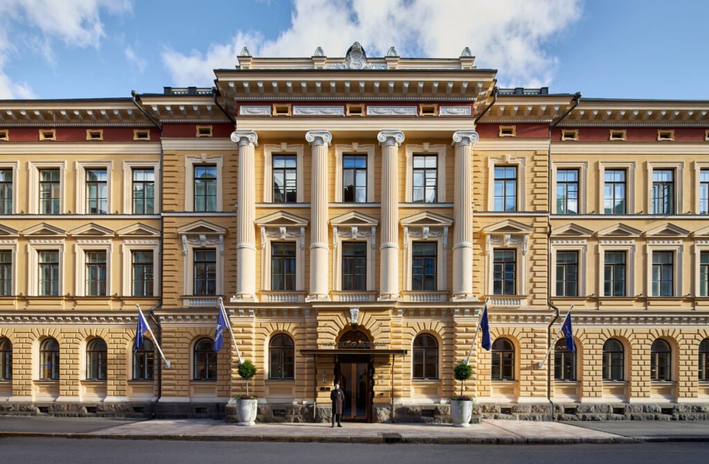 Front exterior of Waldorf Astoria Helsinki with columns and flags.
