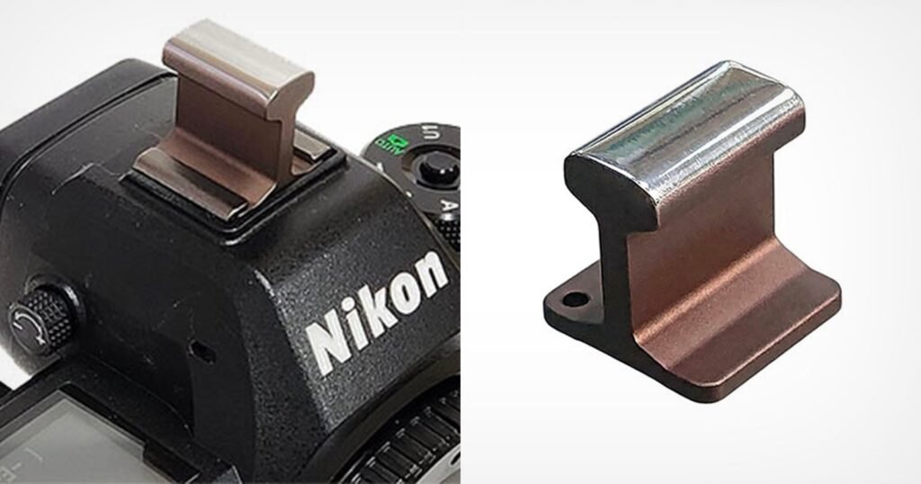 A metal accessory shaped like a miniature railroad rail, shown installed on the hot shoe of a Nikon camera on the left, and separately on the right against a white background.